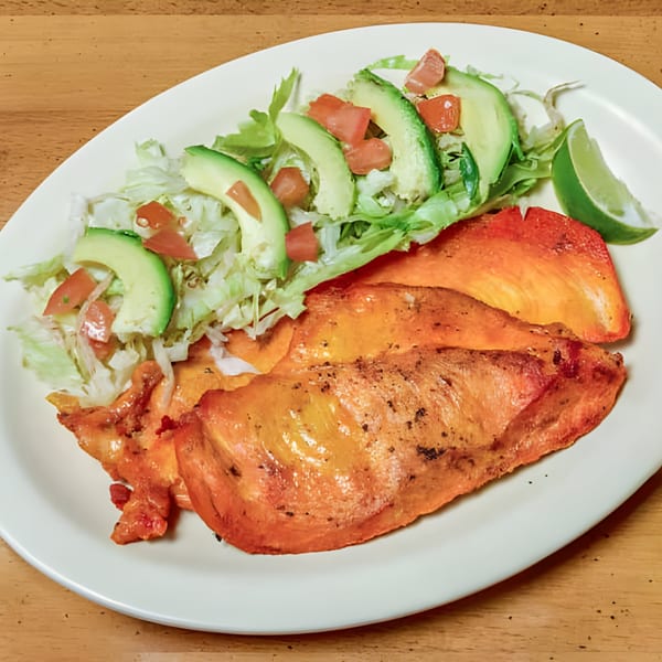 Latin-American grilled chicken with a side salad of lettuce, avocado, tomato, and a lime wedge.