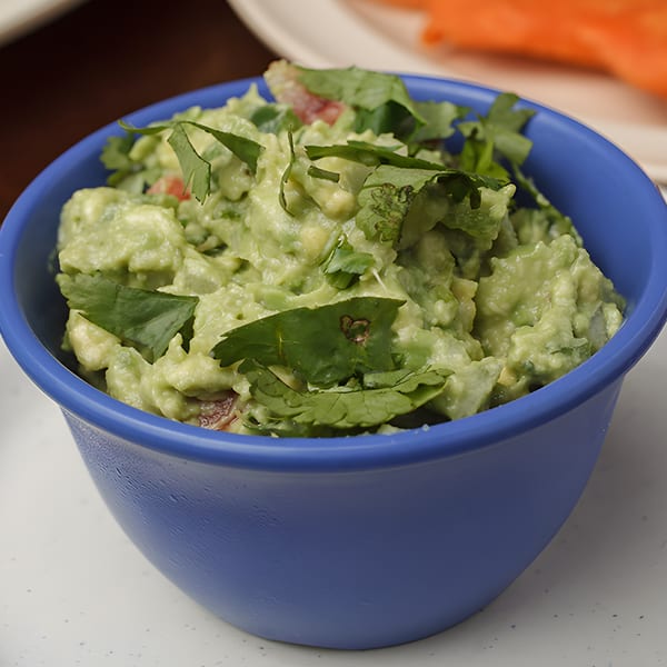 A blue bowl filled with chunky guacamole, garnished with fresh cilantro and diced tomatoes.