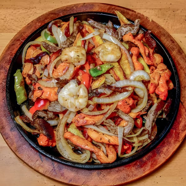 Sizzling El Sabor Latin Cuisine fajitas with shrimp, chicken, beef, onions, and colorful peppers on a wooden platter.