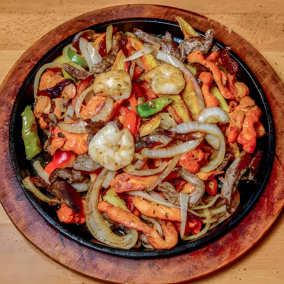 Sizzling El Sabor Latin Cuisine fajitas with shrimp, chicken, beef, onions, and colorful peppers on a wooden platter.