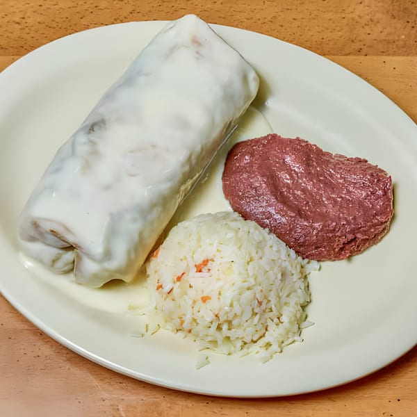 A Latin-American burrito covered in white sauce, served with rice and refried beans on a white plate.