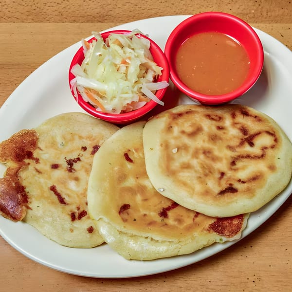 Three golden-brown pupusas with curtido and salsa roja in red bowls on a white plate.