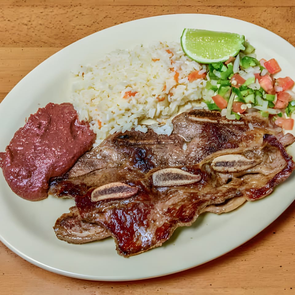 Grilled short ribs, rice, refried beans, pico de gallo, and a lime wedge on a plate.